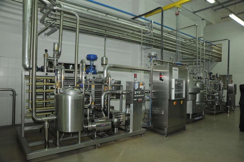 Imagem interna da fábrica mostrando o pasteurizador (mais à esquerda) e a desnatadeira por centrifugação (à direita)